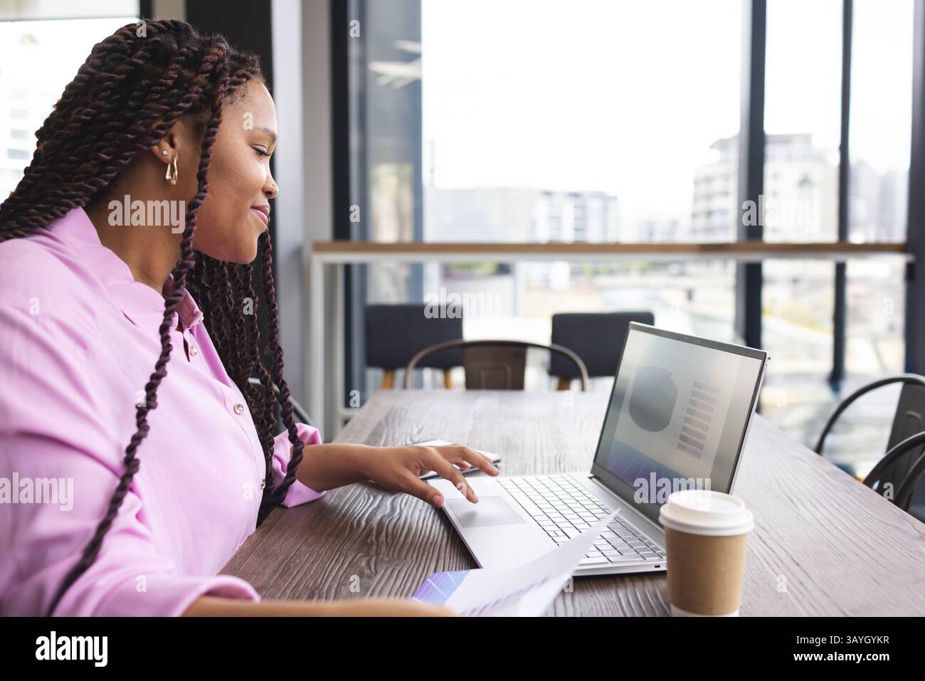 Femme tapant sur ordinateur portable à l'espace de coworking moderne, tenant le document et la tasse à café Banque D'Images