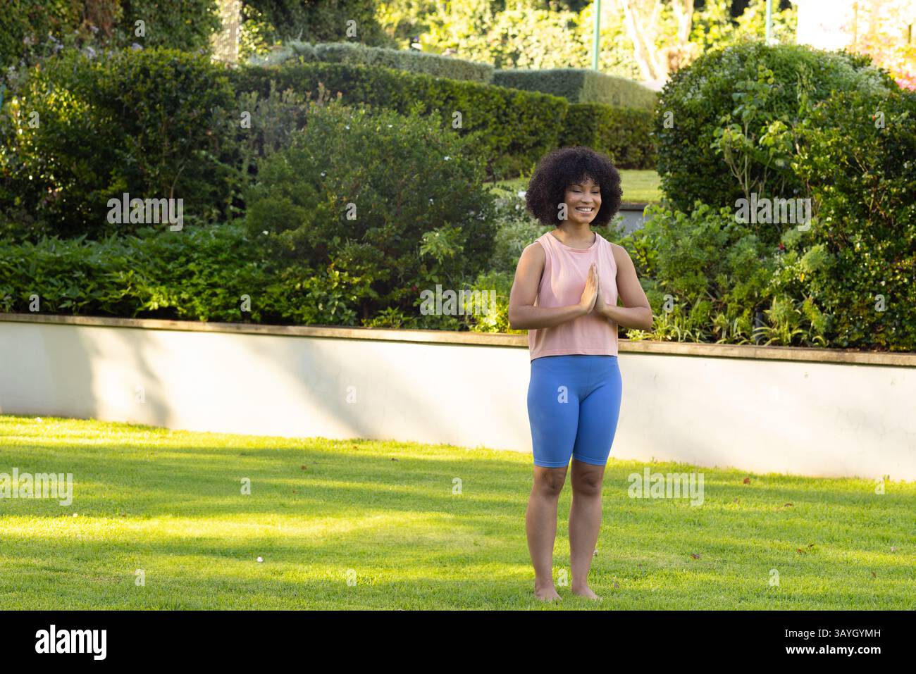Femme pratiquant le yoga pose sur la pelouse bien entretenue dans le jardin avec mur de béton et haies, espace de copie Banque D'Images