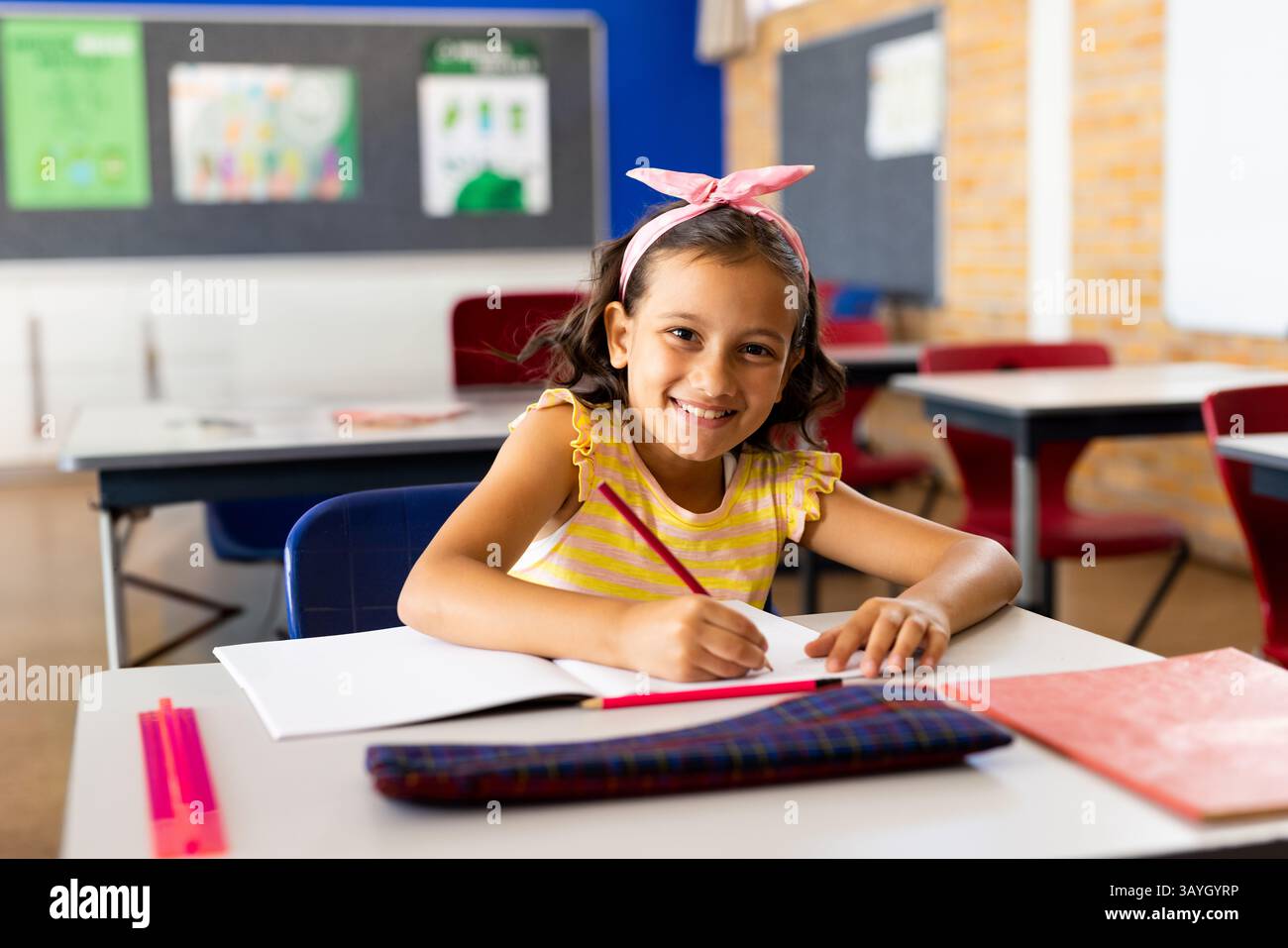 fille de 7 ans écrivant dans une salle de classe élémentaire, avec un cahier ouvert, un crayon rouge et une règle rose Banque D'Images