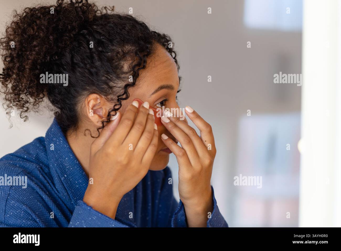 Femme appliquant un patch rouge de soin sous les yeux à l'intérieur, mettant en valeur la routine d'auto-soin Banque D'Images