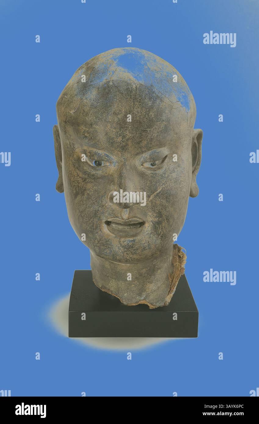 Une grande sculpture en pierre altérée d'une tête humaine, avec des détails faciaux complexes, tels que des sourcils sillonnés et des oreilles distinctes, montée sur une base noire élégante. La surface montre des signes d'âge et d'usure, avec des taches de bleu et des imperfections naturelles ajoutant à son caractère. Chef d'une dynastie Luohan, Song du Nord, Liao, ou Jin, c. XIe siècle, Chine, laque sèche creuse, 28,6 × 18 × 20 cm (11 1/4 × 7 1/16 × 7 7/8 po.) Art classique avec une touche moderne réinventé par Artotop Banque D'Images