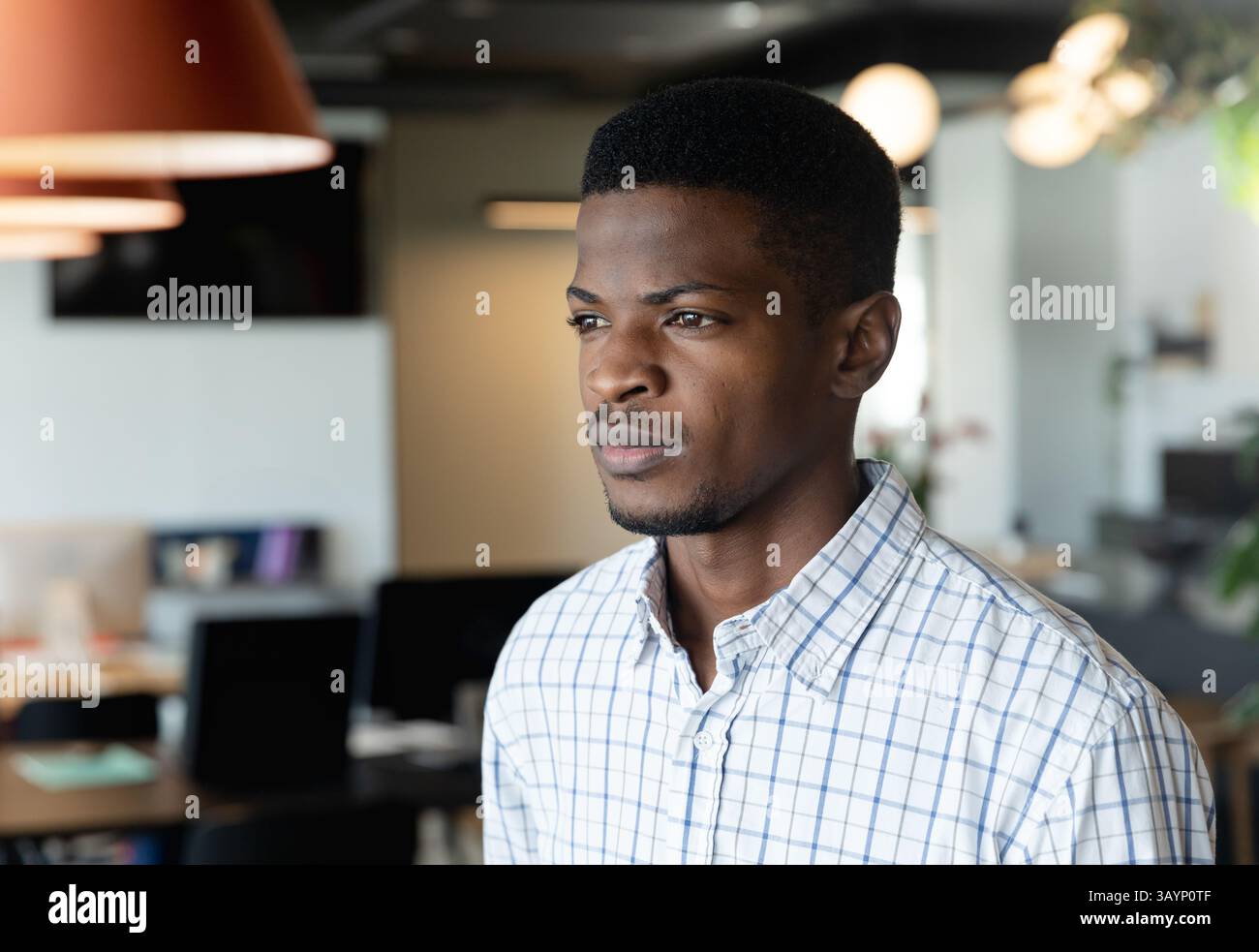 Homme afro-américain debout dans un bureau ouvert, avec des écrans d'ordinateur et des bureaux, espace de copie Banque D'Images