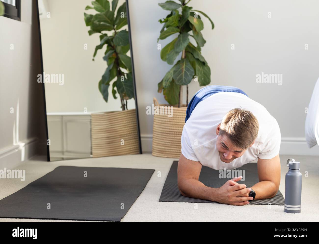 Homme tenant la planche de l'avant-bras sur le tapis de yoga à la maison, avec bouteille d'eau de plante miroir, espace de copie Banque D'Images
