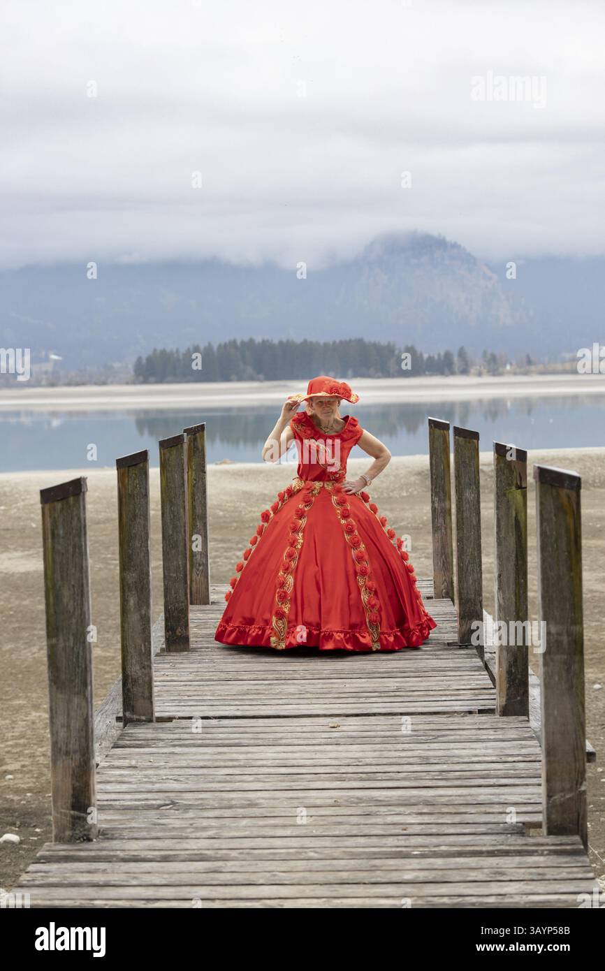 Femme dans une robe rouge debout sur une jetée, Forggensee, Allgaeu, Bavière, Allemagne, Europe Banque D'Images