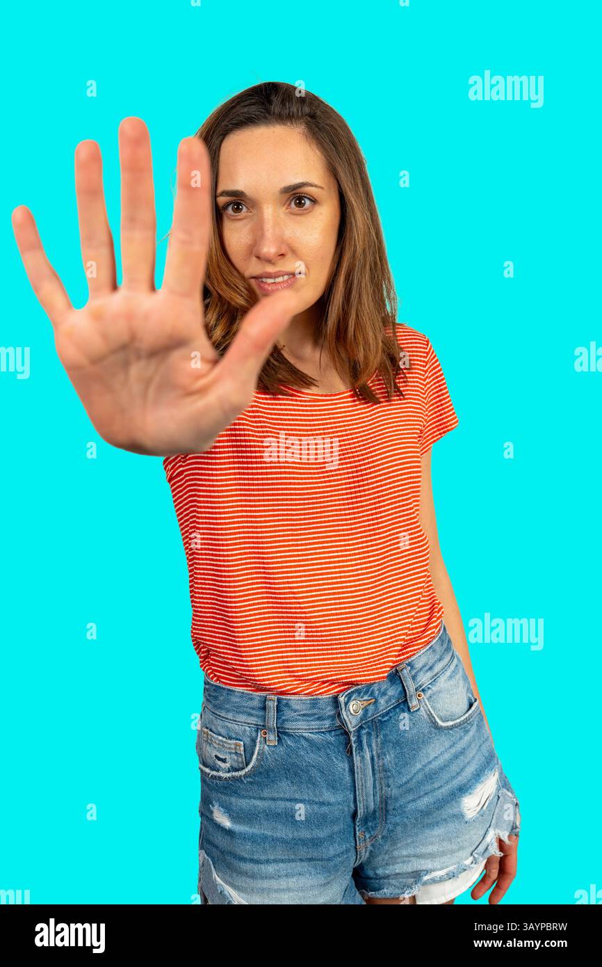 Jeune femme montrant un geste stop avec sa main sur un fond turquoise, exprimant confiance et affirmation de soi Banque D'Images