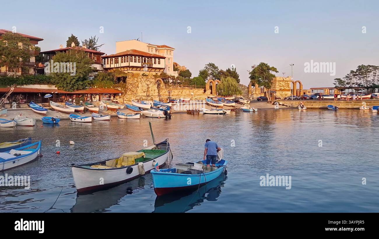 Scène portuaire sereine dans la lumière chaude du coucher du soleil, de nombreux petits bateaux flottent sur l'eau calme. Bâtiments historiques traditionnels et ruines antiques de la vieille ville Banque D'Images