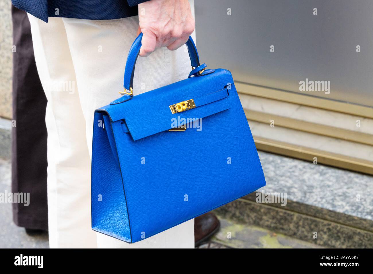 Milan, Italie - 12 avril 2025 : Street style. Femme élégante tenant un sac à main Hermes en cuir bleu vif structuré avec du matériel en or. Détail mode Banque D'Images