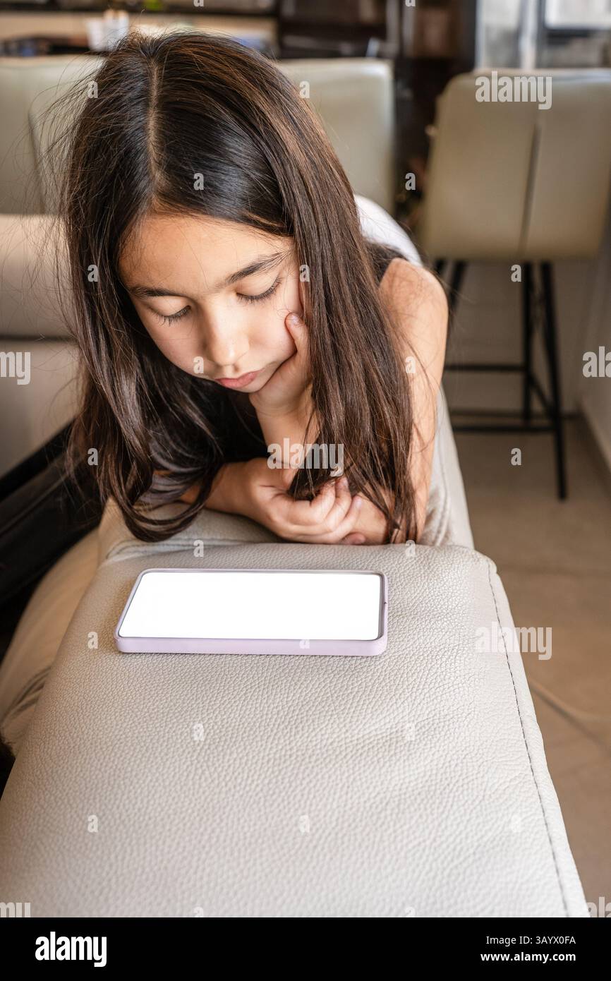 Generation Alpha Girl allongée sur un canapé avec une tablette vierge, parfaite pour une utilisation maquette, symbolisant l'apprentissage numérique précoce et la présence croissante de l'IA dans la vie des enfants. Banque D'Images