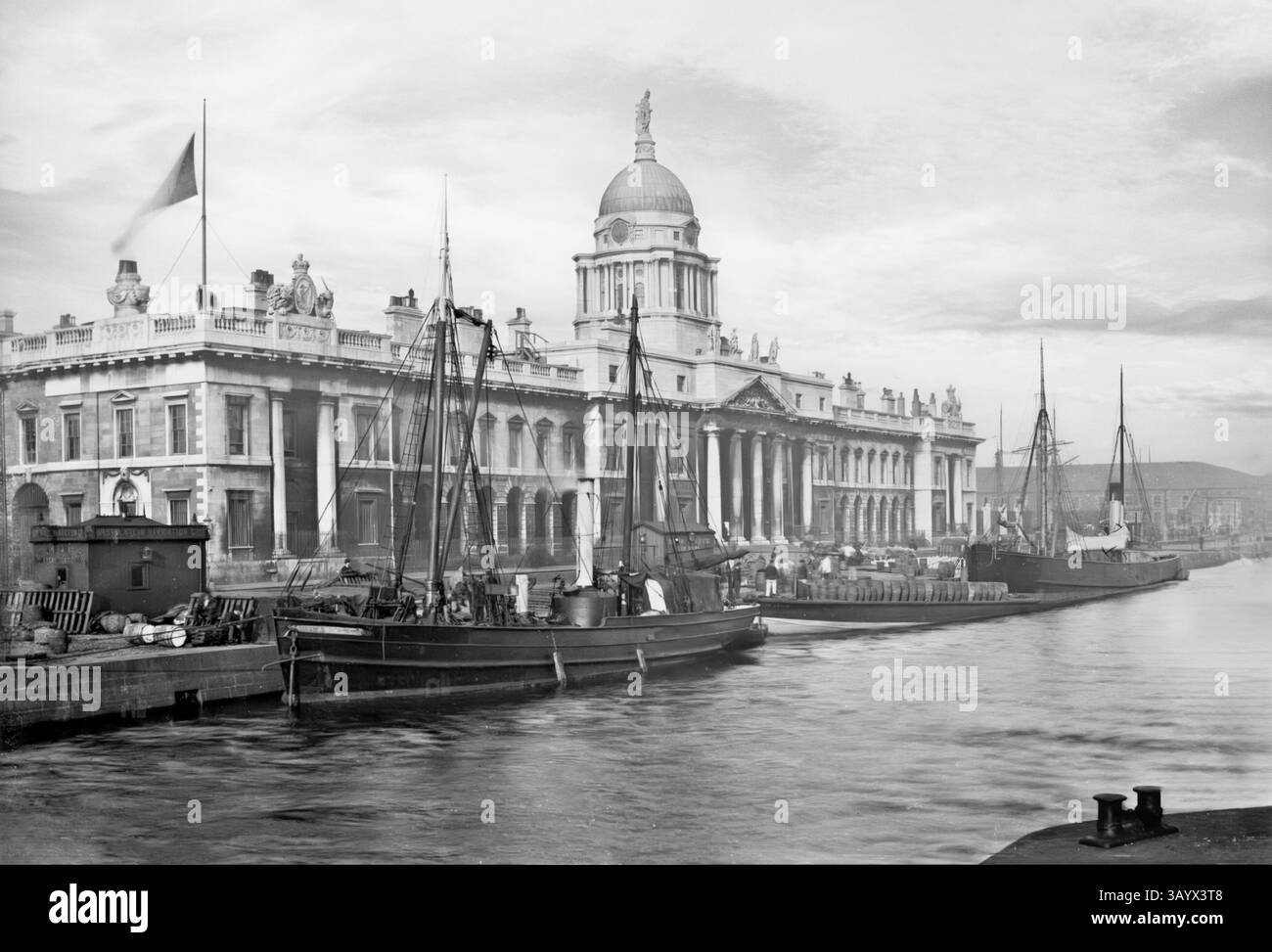 Une vue du début du XXe siècle de navires amarrés le long de la maison de douane néoclassique du XVIIIe siècle sur la rivière Liffey, Dublin, Irlande. La construction a commencé en 1781 et James Gandon a été nommé architecte, après la mort de Thomas Cooley, l'architecte original du projet. Une fois achevé et ouvert aux entreprises le 7 novembre 1791, il avait coûté £200 000 à construire – une somme considérable à l’époque. Les quatre façades du bâtiment sont décorées d'armoiries et de sculptures ornementales (d'Edward Smyth) représentant les rivières irlandaises. Banque D'Images