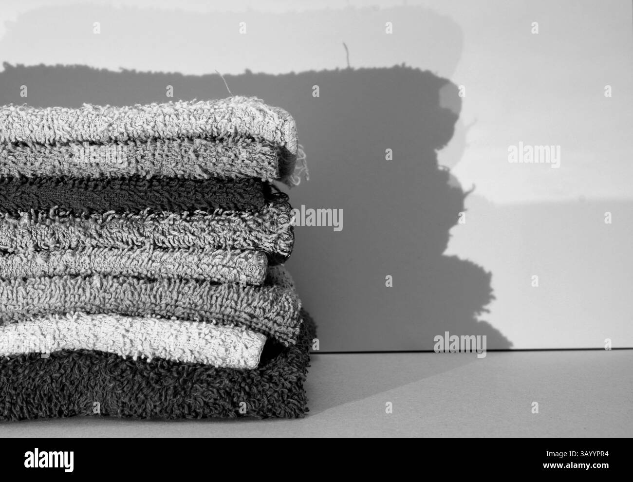 Une pile noire et blanche de gants de toilette pliés, avec leur ombre sur le mur derrière eux. Banque D'Images