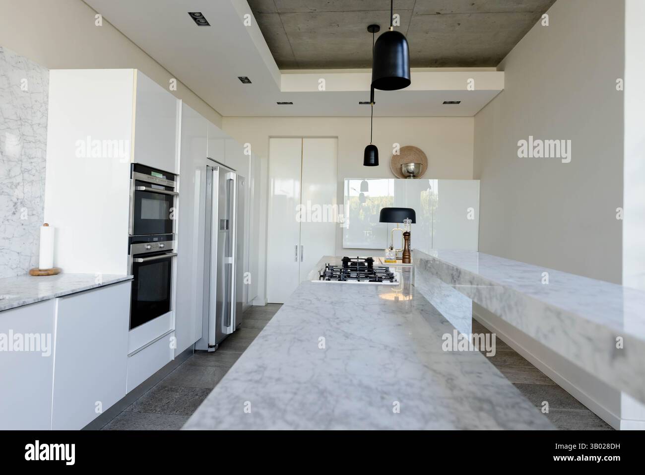 L'îlot de cuisine en marbre ancre la cuisine minimaliste avec une table de cuisson à gaz et des suspensions noires Banque D'Images