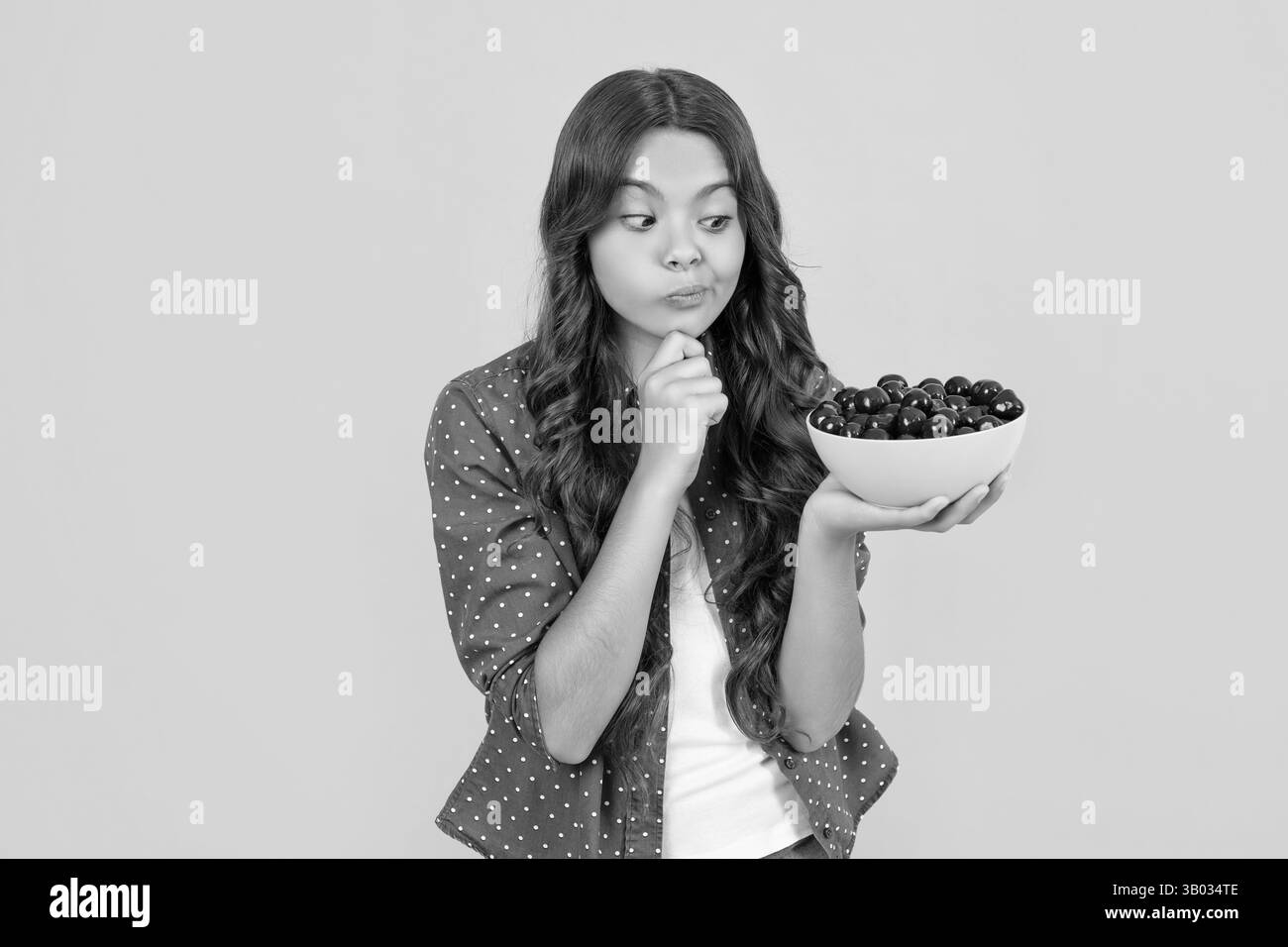 une jeune fille attentionnés tient un bol de cerise sur fond jaune Banque D'Images