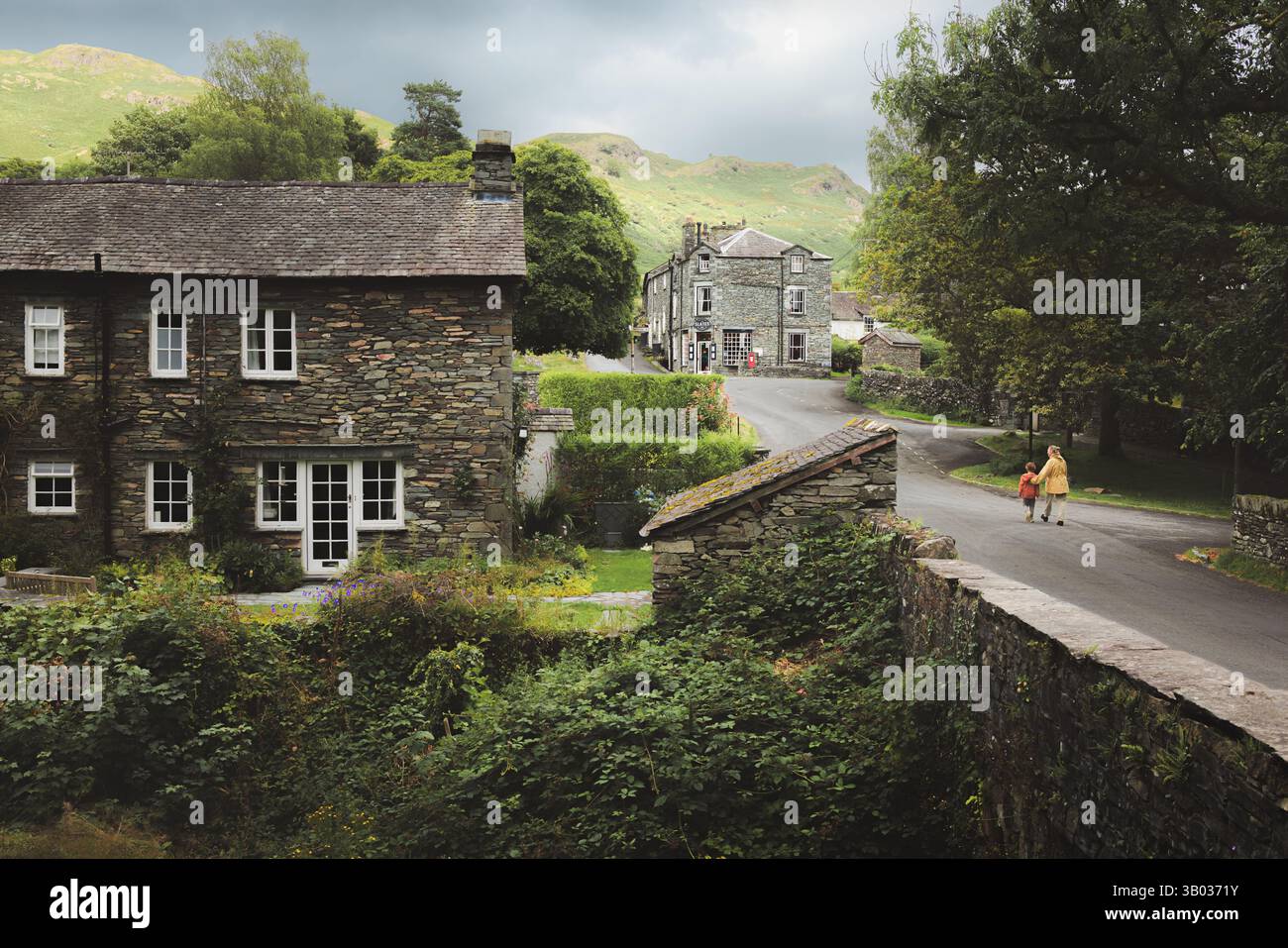 Elterwater, Royaume-Uni - 9 août 2024 : une mère et son fils se promènent dans le charmant village d'Elterwater, entouré de cottages historiques en pierre d'ardoise et se Banque D'Images