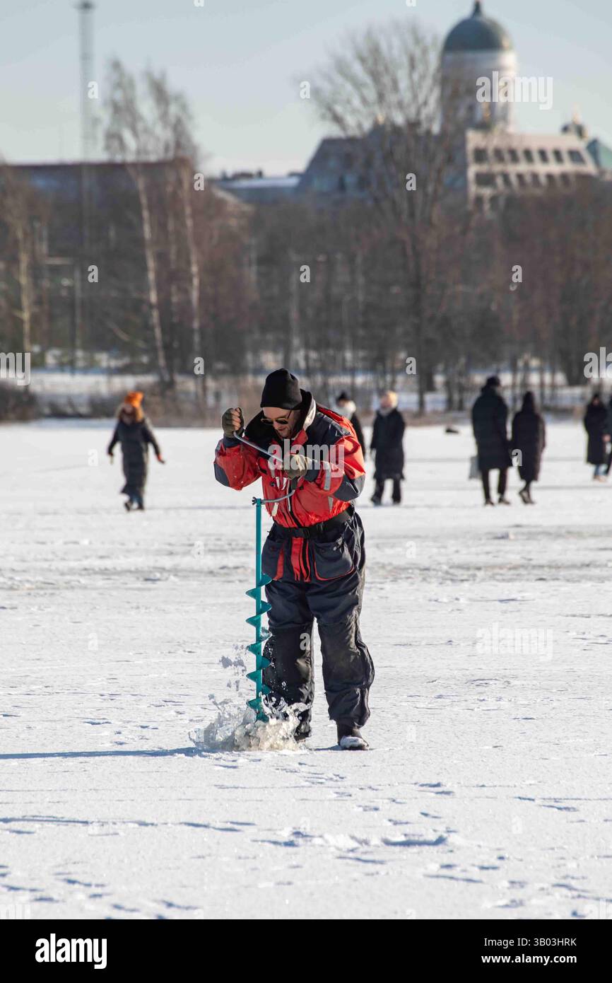 pêcheur de glace perçant un trou de pêche sur glace avec une tarière sur la baie gelée de Töölönlahti à Helsinki, Finlande Banque D'Images