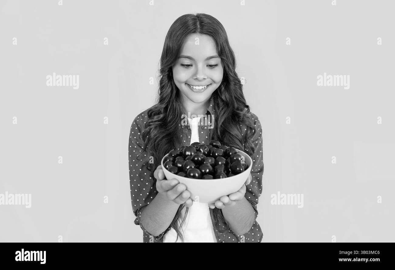 une jeune fille positive tient un bol de cerise sur fond jaune Banque D'Images