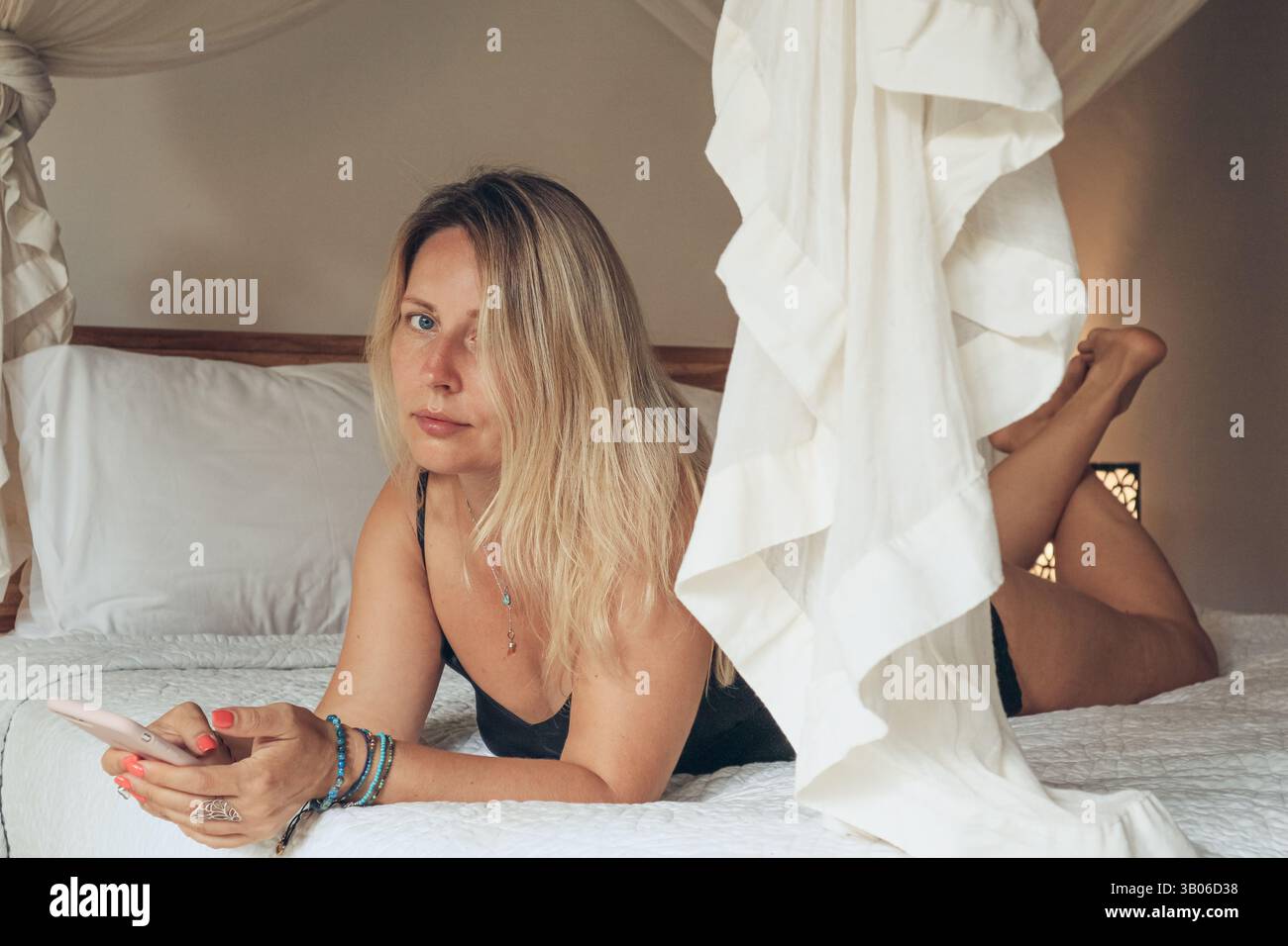 Belle femme blonde à l'aide d'un smartphone couché sur le lit dans la chambre Banque D'Images