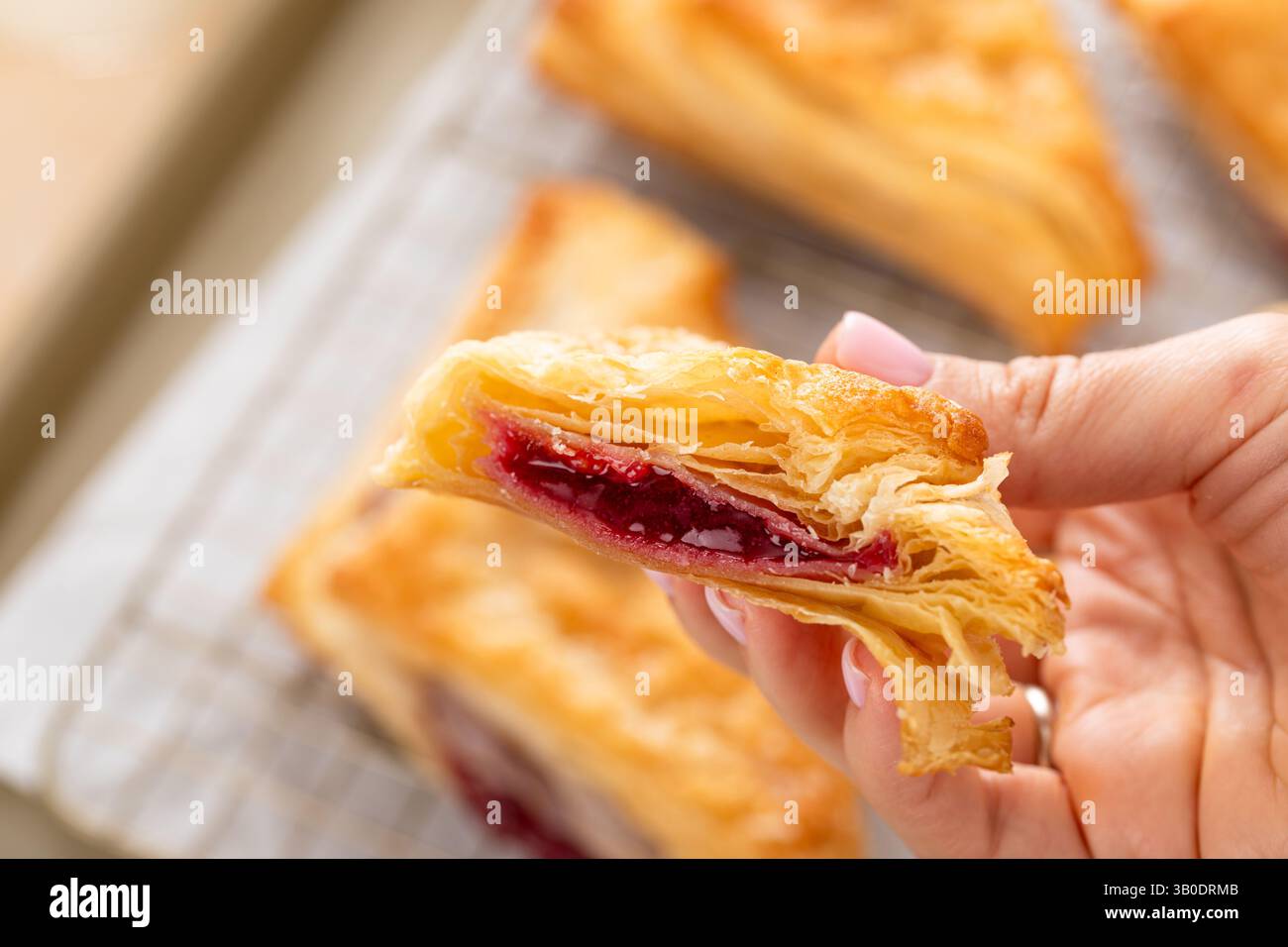 Pâtisseries feuilletées avec de la confiture de cerises ou de baies sur une plaque à pâtisserie fraîchement cuite coupée en deux pour montrer la garniture Banque D'Images