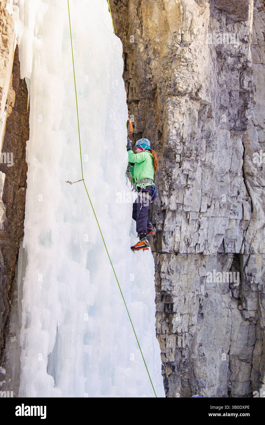 Canmore, Alberta Canada - 22 janvier 2022 : une femme grimpant sur la glace une cascade utilisée pour l'entraînement à Grotto Canyon par une chaude journée d'hiver. Banque D'Images