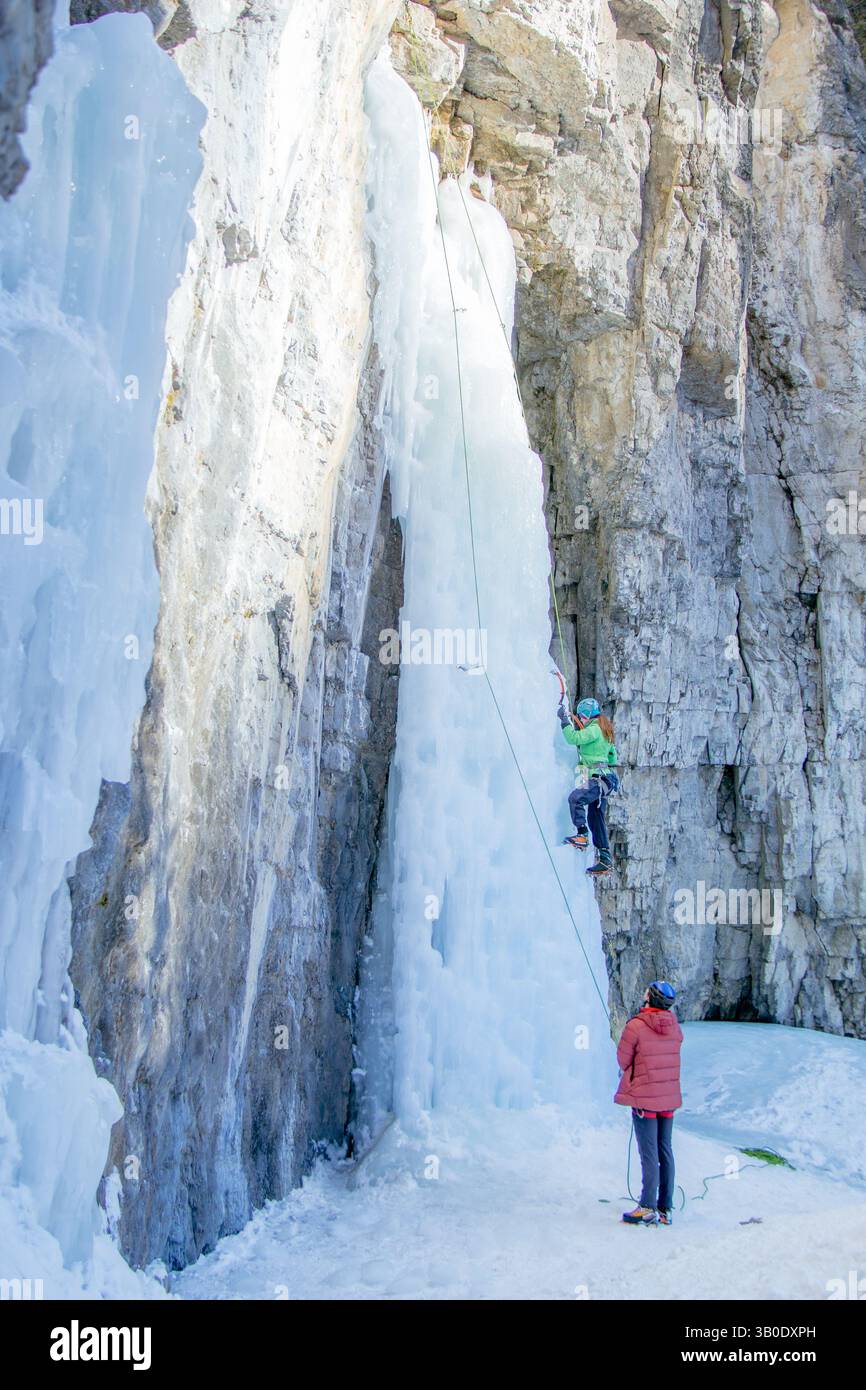 Canmore, Alberta Canada - 22 janvier 2022 : un homme et une femme grimpant sur la glace une cascade utilisée pour l'entraînement à Grotto Canyon par une chaude journée d'hiver. Banque D'Images