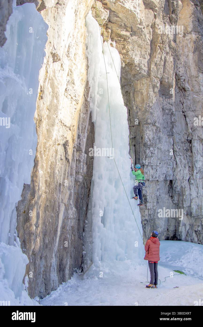 Canmore, Alberta Canada - 22 janvier 2022 : un homme et une femme grimpant sur la glace une cascade utilisée pour l'entraînement à Grotto Canyon par une chaude journée d'hiver. Banque D'Images