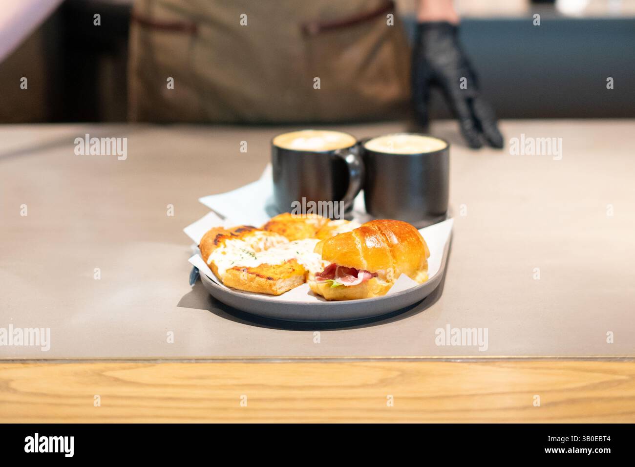 Le barista sert des sandwichs gastronomiques frais pour le petit déjeuner accompagnés d'un café artisanal dans un cadre de café branché, capturant les vibrations chaleureuses du brunch et la présentation de la nourriture Banque D'Images