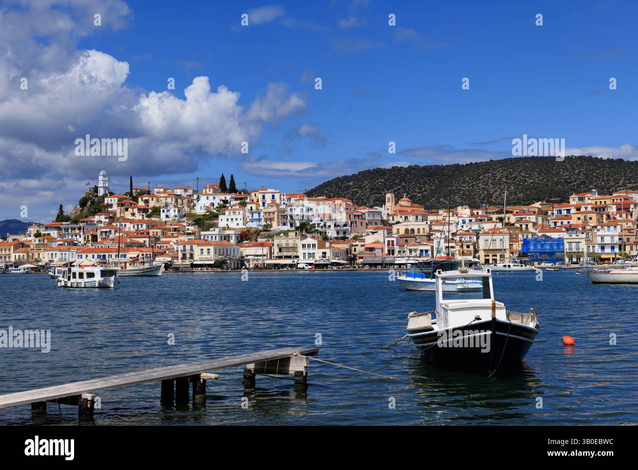 Bateau de pêche traditionnel flottant dans la mer bleue près de la ville côtière colorée de Poros, en Grèce, sous un ciel lumineux. Représentation parfaite du grec Banque D'Images