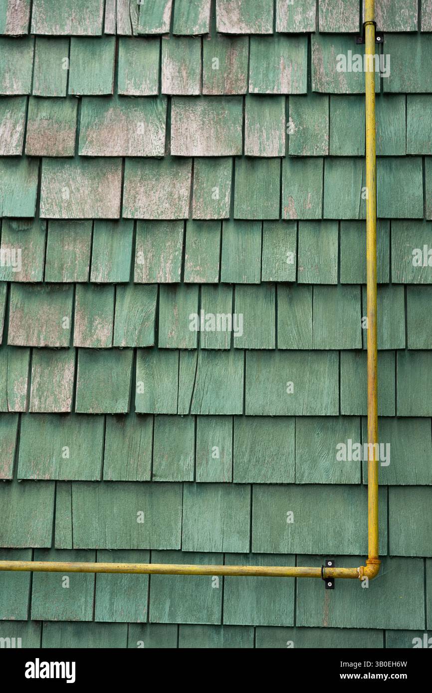 tuyau d'évacuation rouillé jaune fixé ou fixé à l'extérieur extérieur du mur de bardeaux ou de shake peint en vert décoloration et écaillage rustique texturé Banque D'Images