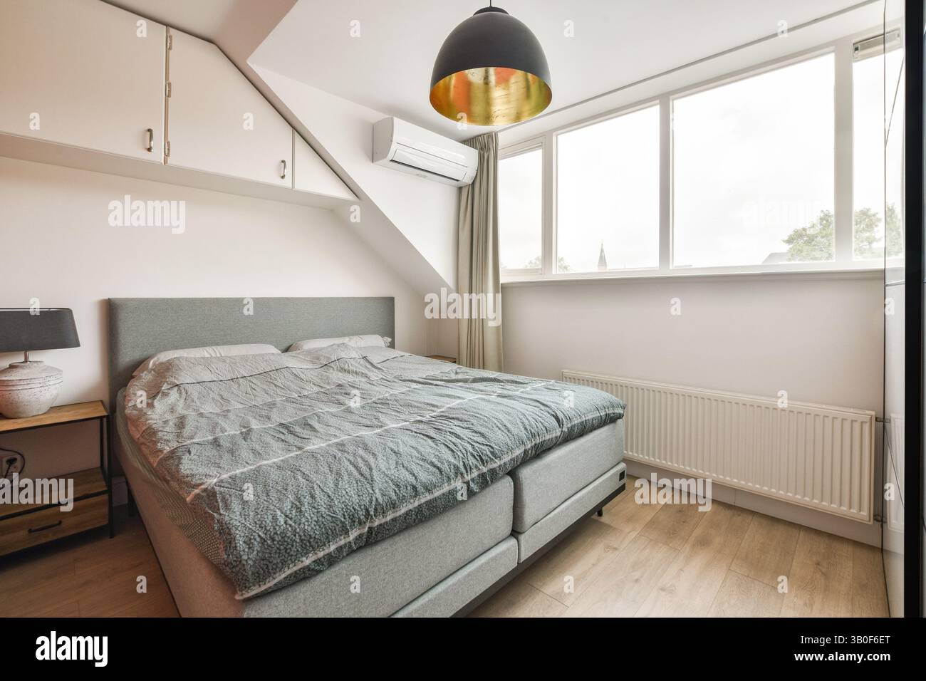 Une chambre moderne confortable avec un lit confortable, un décor élégant et de grandes fenêtres permettant à la lumière naturelle de remplir l'espace, créant une atmosphère sereine. Banque D'Images