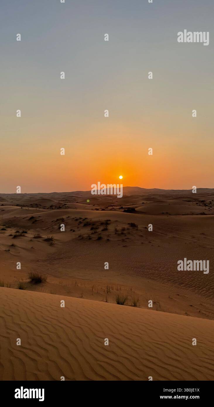 Coucher de soleil à couper le souffle sur les dunes dorées du désert, mettant en valeur la beauté paisible de la nature dans le paysage arabe - Image de stock capturée avec un smartphone