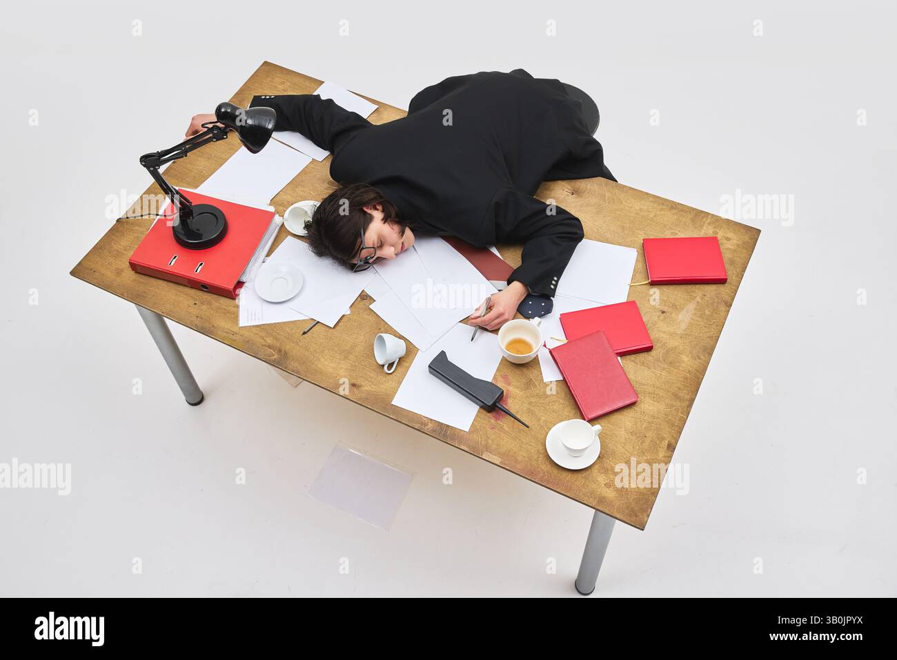 Vue aérienne d'un employé épuisé s'est effondré sur un bureau encombré avec du café renversé et des documents éparpillés. Banque D'Images