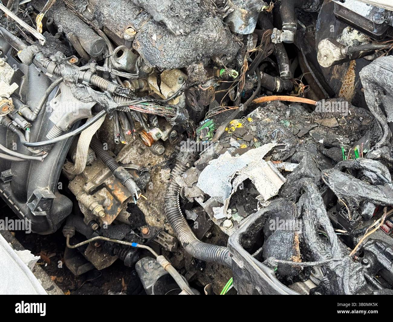 Bloc-moteur et câblage brûlés avec couvercles en plastique fondu, connecteurs carbonisés et composants exposés après de graves dommages causés par un incendie dans le compartiment moteur. Banque D'Images