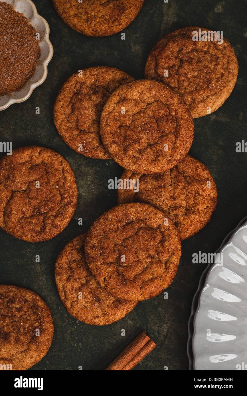 Biscuits à la cannelle avec dessus craquelé disposés sur une surface de cuisson sombre. Des vues partielles des ustensiles de cuisson en céramique blanche sont visibles dans les coins. Banque D'Images