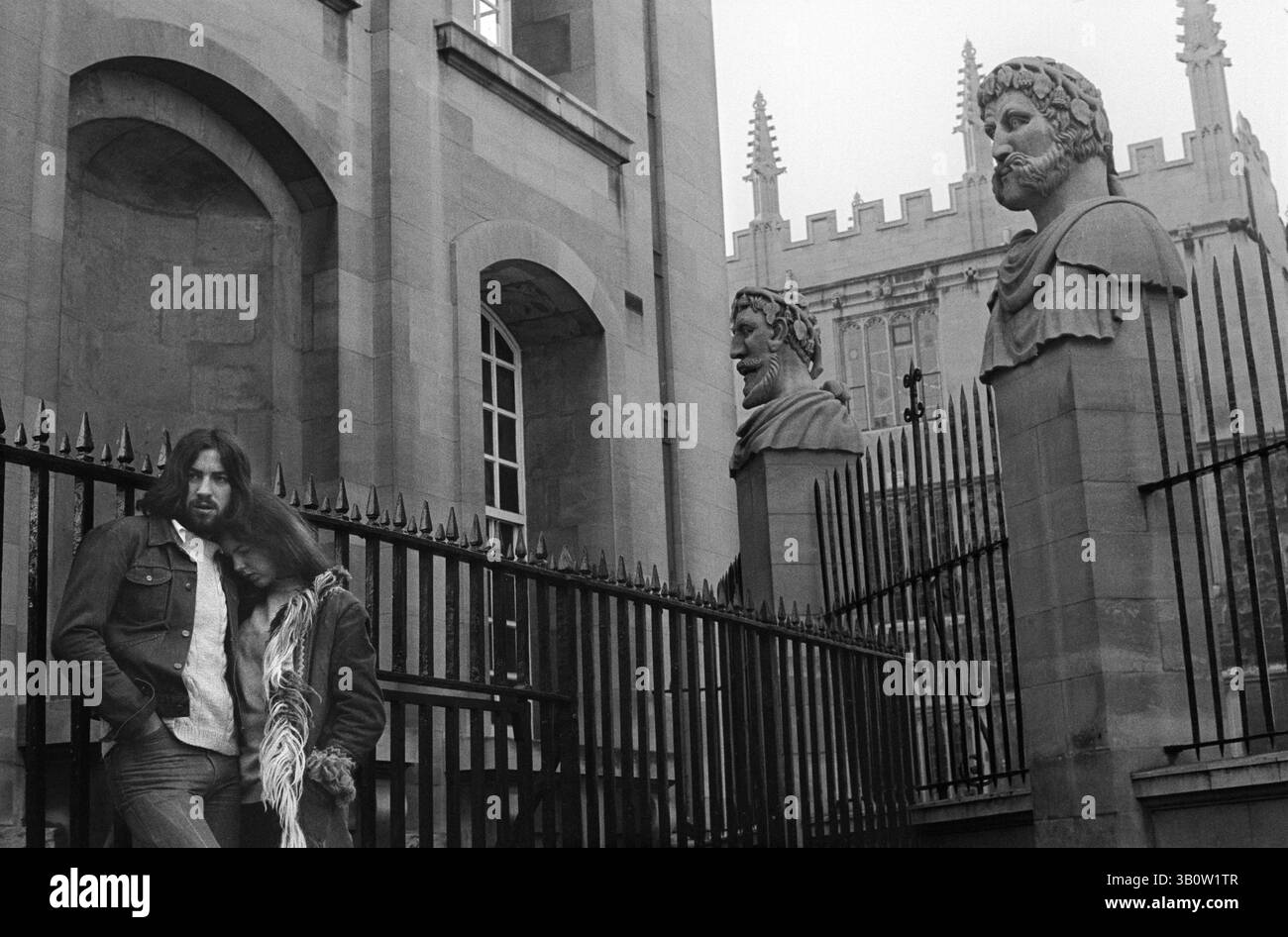 Jour de mai matin Oxford 1976. Le couple froid et sans doute fatigué ayant été debout toute la nuit pour voir l'aube lever du soleil le premier mai. Ils sont à l'extérieur du Clarendon Building de Hawksmoor dans Broad Street. Les deux têtes sont issues d'un groupe de 13 têtes sculptées qui entourent le périmètre du Sheldonian Theatre sont une caractéristique emblématique de Oxford 1970s UK Oxfordshire England 1976 HOMER SYKES Banque D'Images