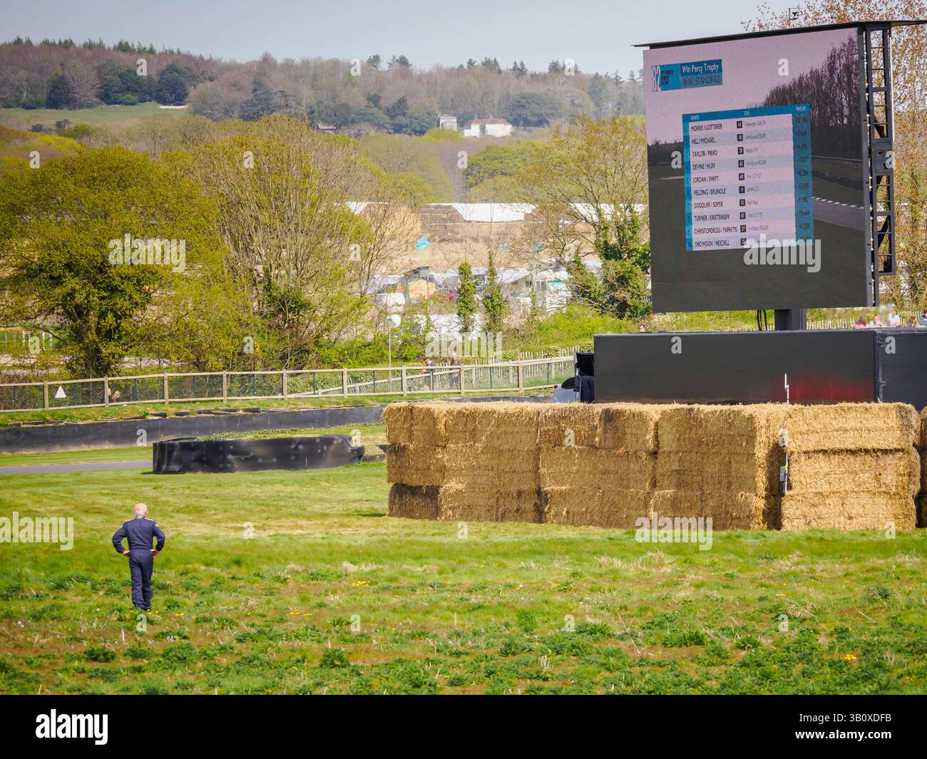 Un conducteur d'une voiture en panne debout seul dans un champ regardant un grand écran, réunion des membres 82, Goodwood Motor circuit, West Sussex UK Banque D'Images