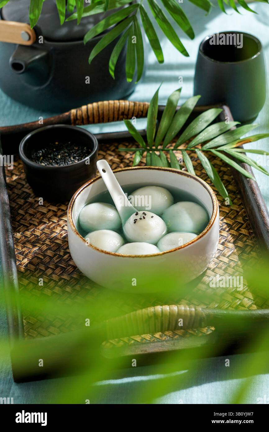 Tang Yuan, dessert asiatique traditionnel composé de boulettes de riz glutinus au sirop sucré, servi dans un bol avec une cuillère sur un plateau tissé, graines de sésame noir a Banque D'Images