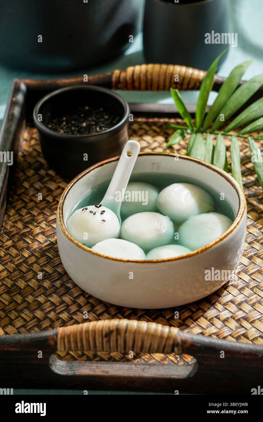 Tang Yuan, dessert asiatique traditionnel composé de boulettes de riz glutinus au sirop sucré, servi dans un bol avec une cuillère sur un plateau tissé, graines de sésame noir a Banque D'Images