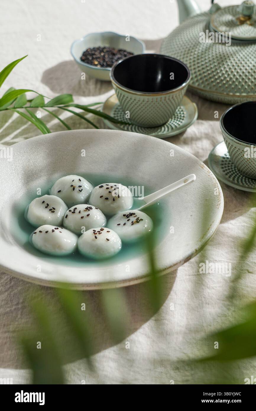 Tang Yuan, dessert asiatique traditionnel composé de boulettes de riz glutinus au sirop sucré, servi dans un bol avec une cuillère, des graines de sésame noir et une théière Banque D'Images