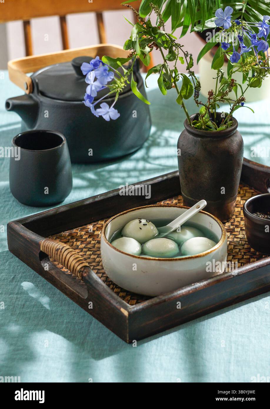 Tang Yuan, dessert asiatique traditionnel composé de boulettes de riz glutinus au sirop sucré, servi dans un bol avec une cuillère sur un plateau tissé, graines de sésame noir a Banque D'Images