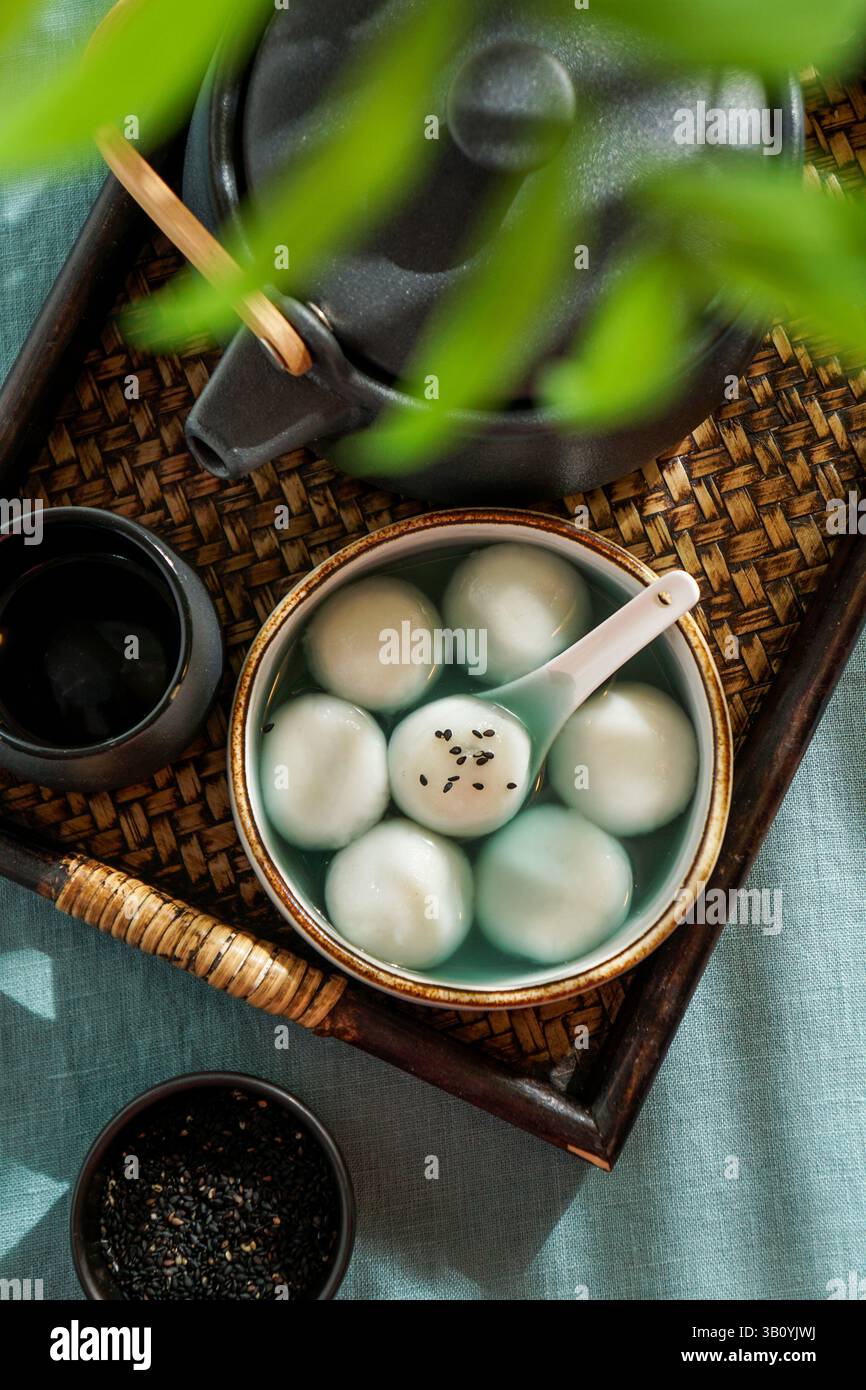 Tang Yuan, dessert asiatique traditionnel composé de boulettes de riz glutinus au sirop sucré, servi dans un bol avec une cuillère sur un plateau tissé, graines de sésame noir a Banque D'Images