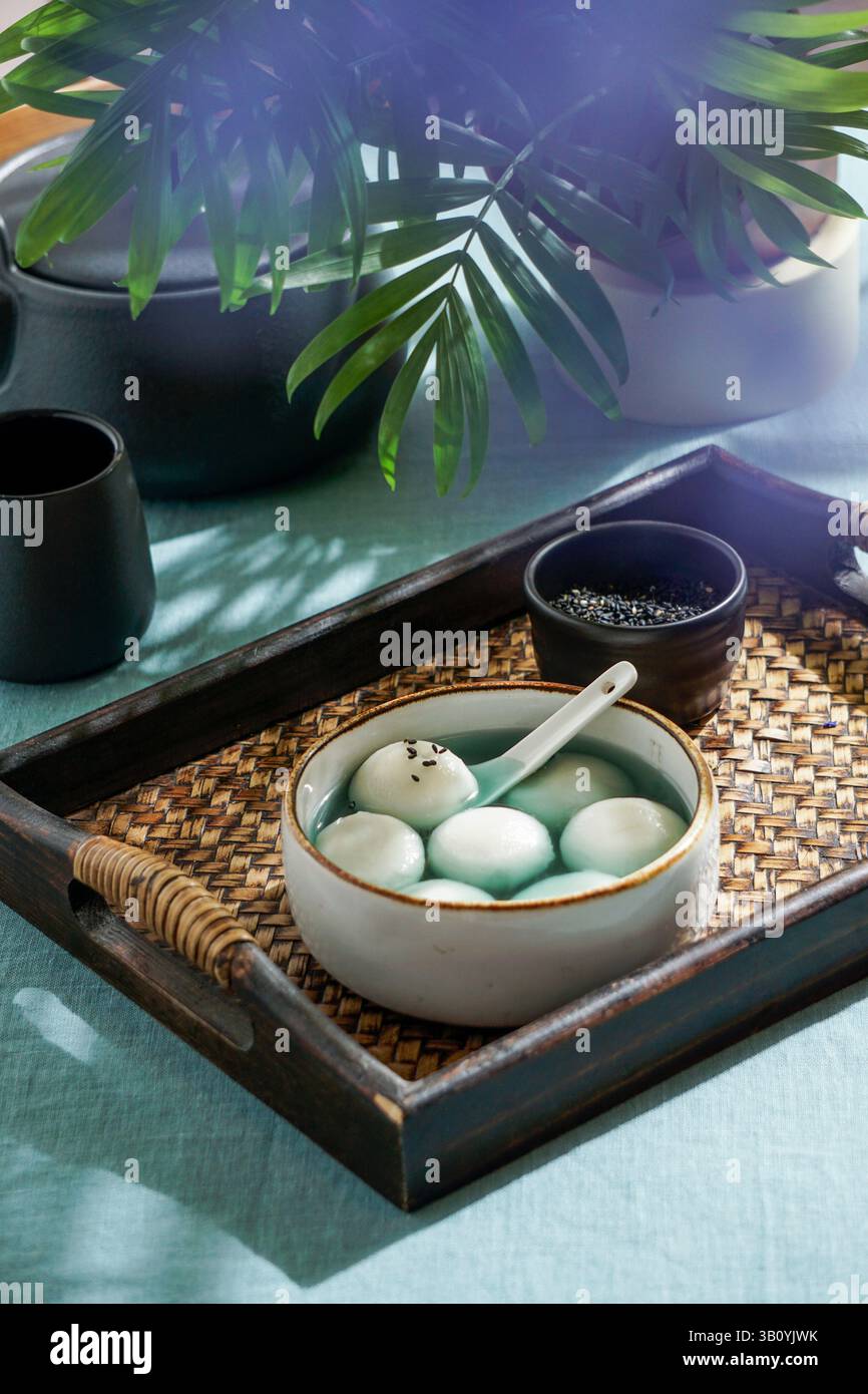 Tang Yuan, dessert asiatique traditionnel composé de boulettes de riz glutinus au sirop sucré, servi dans un bol avec une cuillère sur un plateau tissé, graines de sésame noir a Banque D'Images