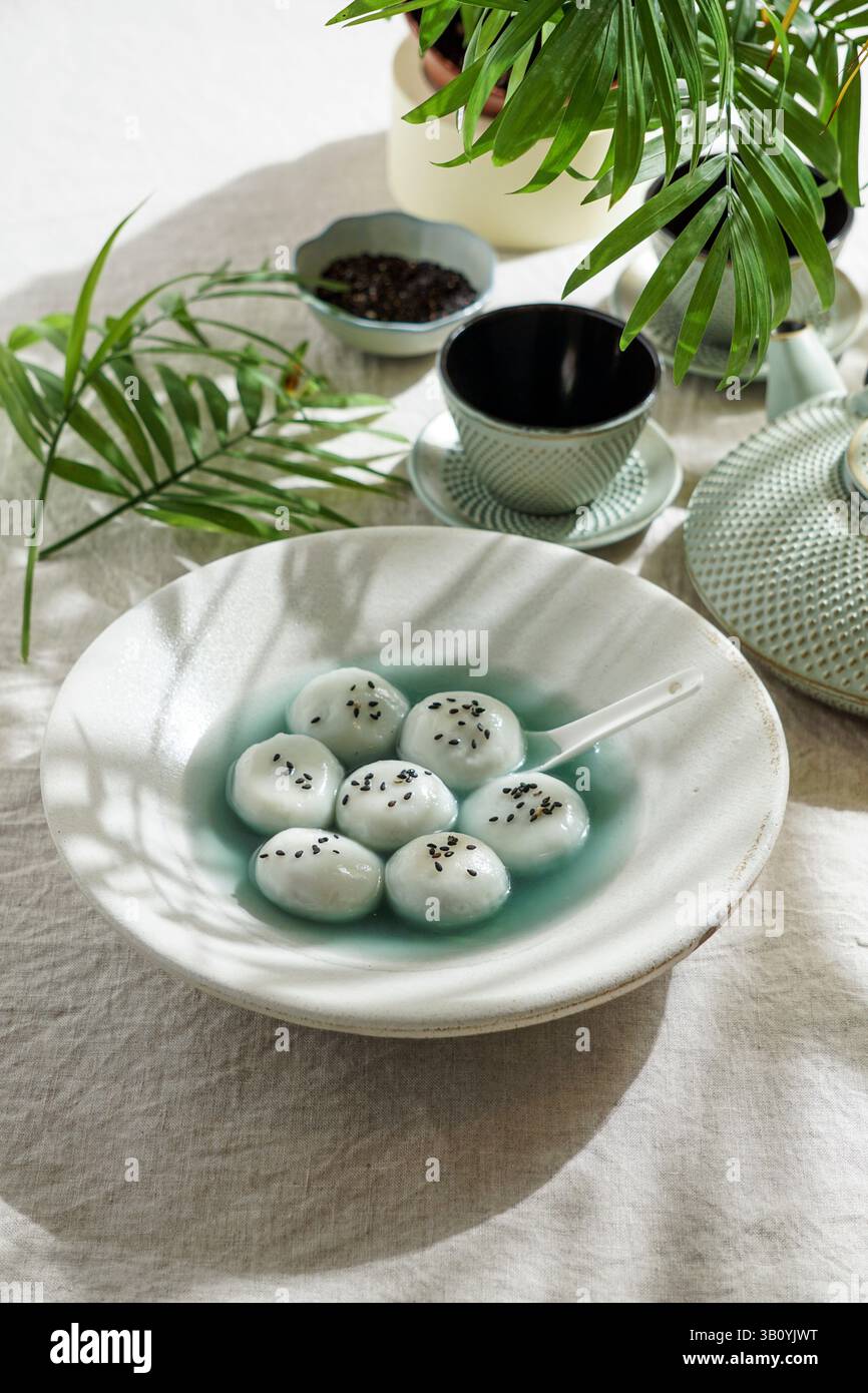 Tang Yuan, dessert asiatique traditionnel composé de boulettes de riz glutinus au sirop sucré, servi dans un bol avec une cuillère, des graines de sésame noir et une théière Banque D'Images