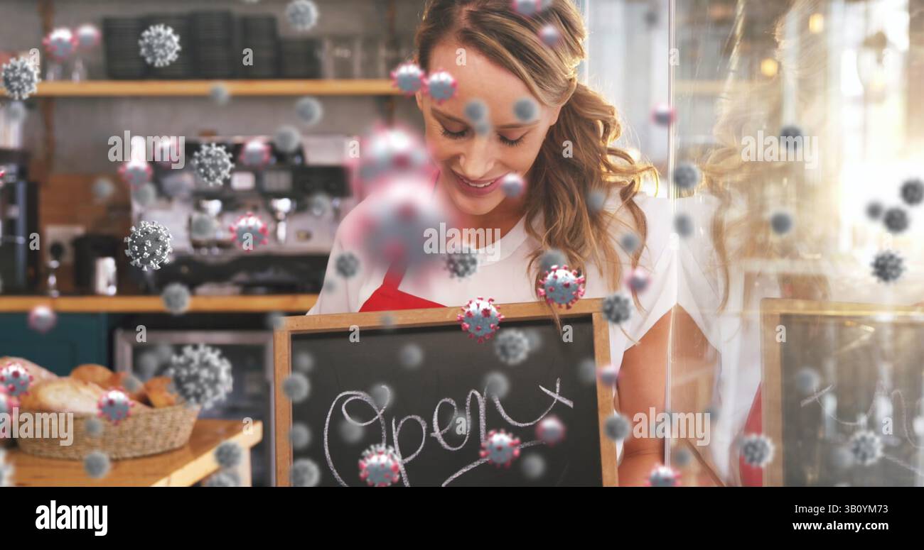 Barista souriant tenant une pancarte ouverte au comptoir du café, avec panier à pain, machine à espresso et virus Banque D'Images