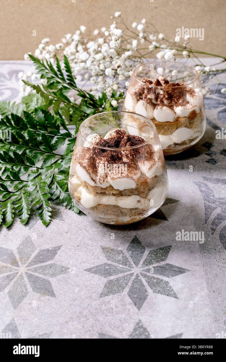 Tiramisu italien classique dans deux verres. Couches de gâteau éponge et crème de mascarpone avec poudre de cacao. Placé sur un carreau à motifs gris-bleu. Bébés blancs Banque D'Images