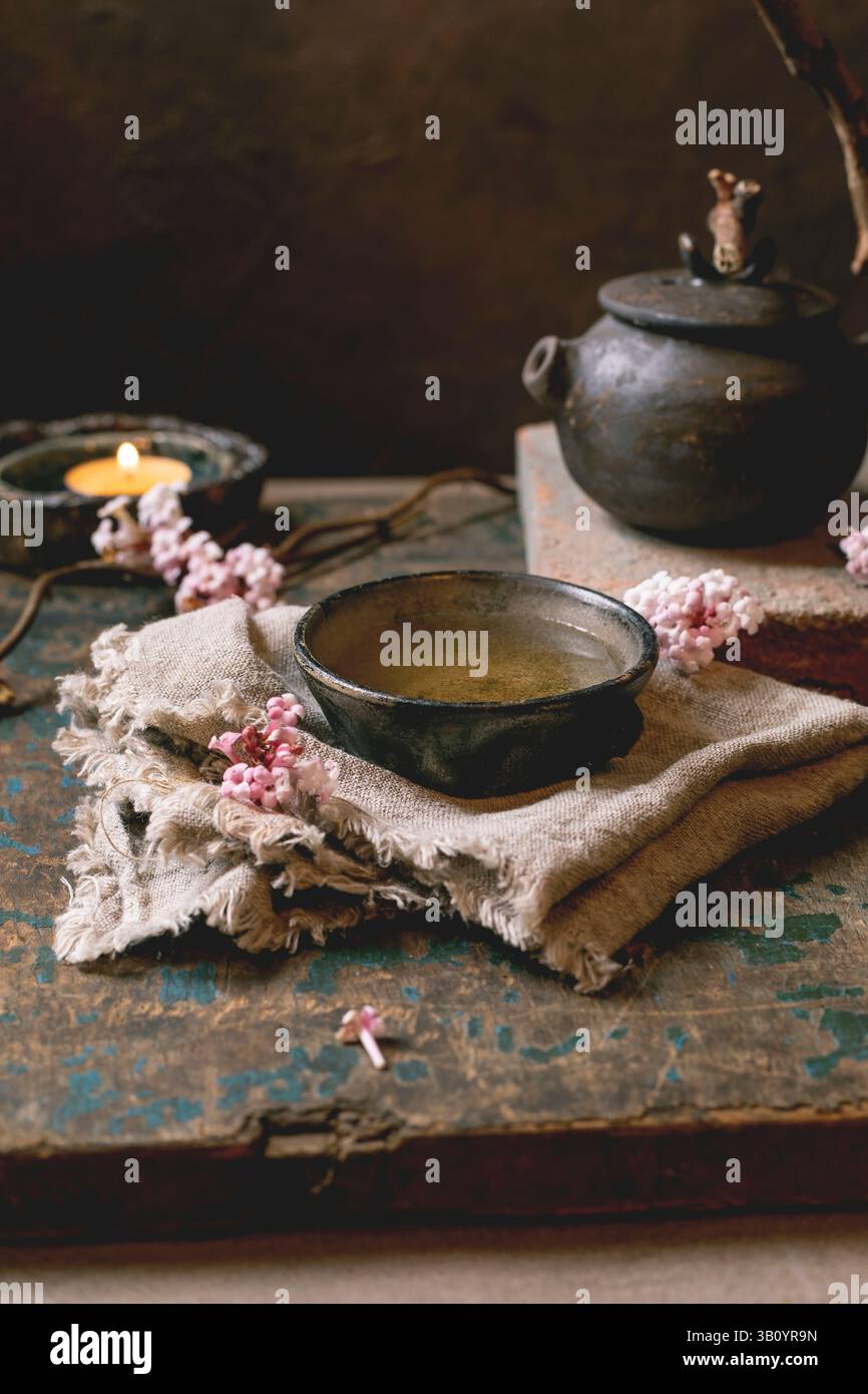 Cérémonie du thé chinois. Théière noire traditionnelle en céramique faite à la main avec poignée en bois sur table en bois foncé. Tasses en céramique et fleurs de printemps roses, brûler Banque D'Images