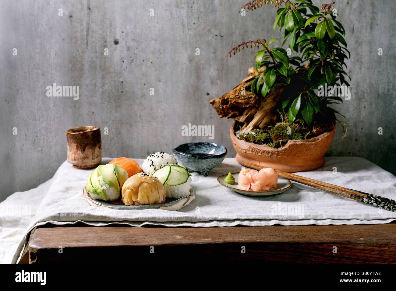 Temari sushi. Boules de sushi tendance avec saumon, avocat, concombre et omelette japonaise sur une assiette wabi-sabi. Sauce soja, gingembre mariné, ikebana sur la table wi Banque D'Images
