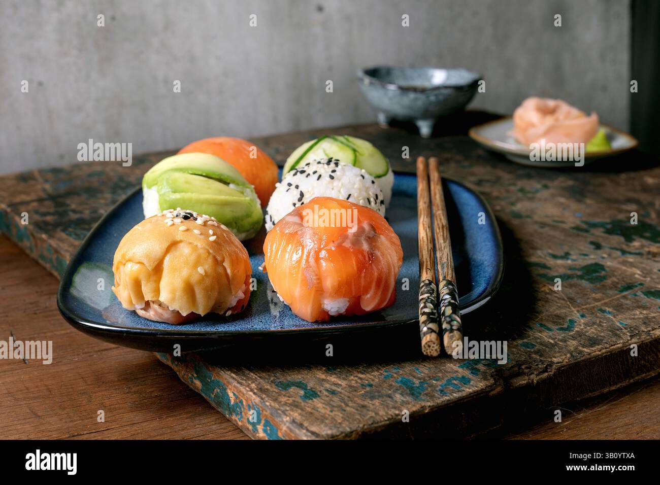 Temari sushi. Boules de sushi tendance avec saumon, avocat, concombre et omelette japonaise sur assiette bleue. Sauce soja, gingembre mariné, baguettes sur WO rustique Banque D'Images