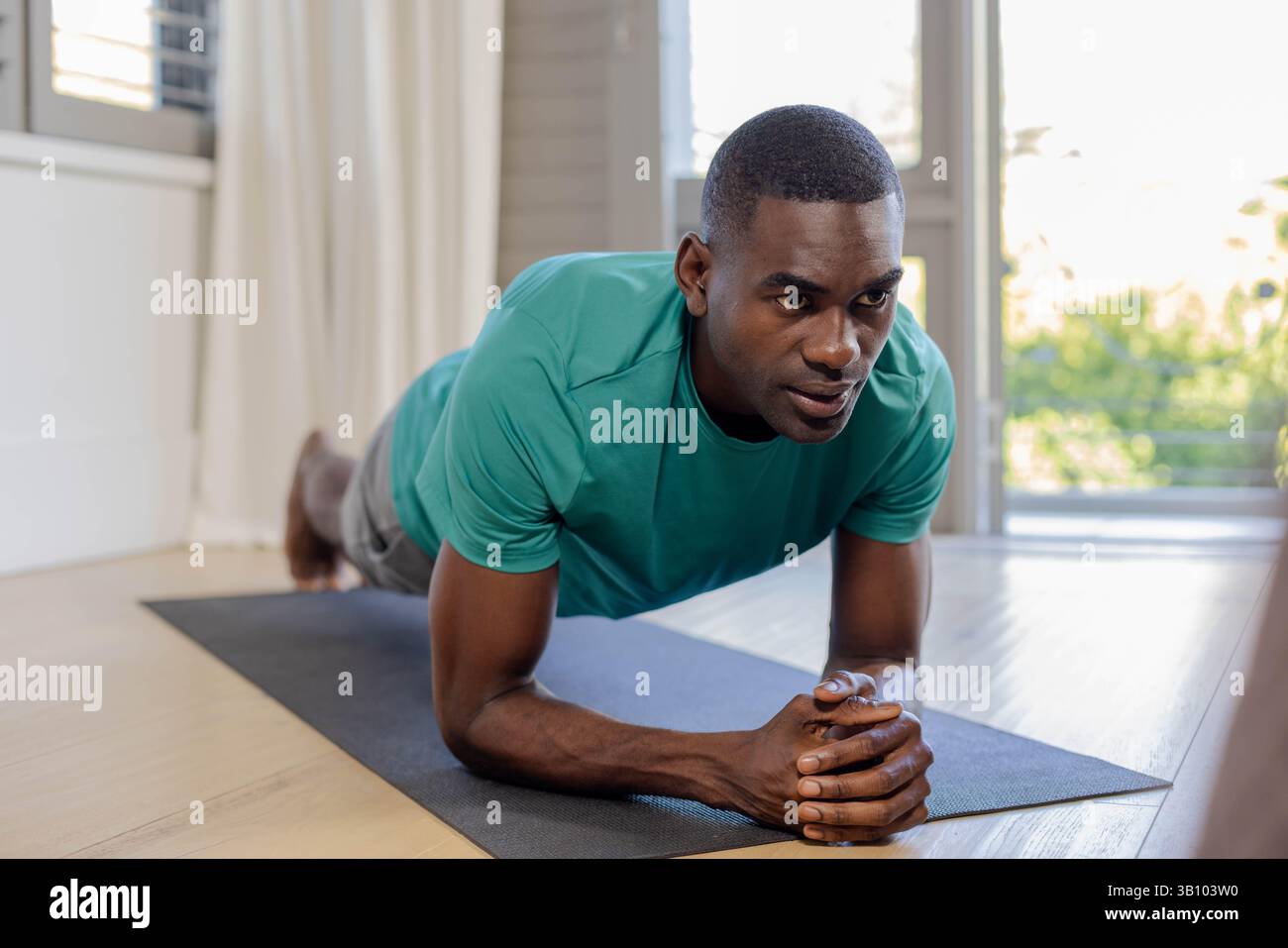 Homme afro-américain faisant planche d'avant-bras sur tapis de yoga à la maison, avec l'accent sur la force Banque D'Images