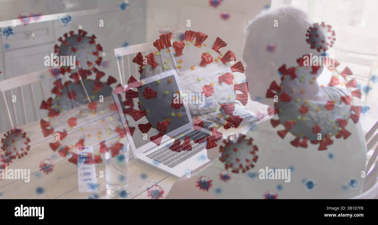 Homme senior travaillant tapant sur ordinateur portable dans la salle à manger, avec verre d'eau, papiers dispersés, espace de copie Banque D'Images