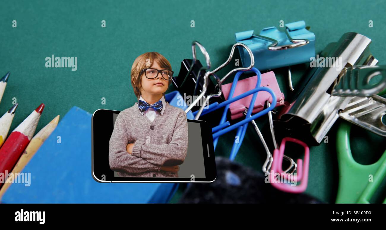 Image d'un écolier caucasien intelligent dans un smartphone se déplaçant sur la papeterie de l'école sur le bureau Banque D'Images