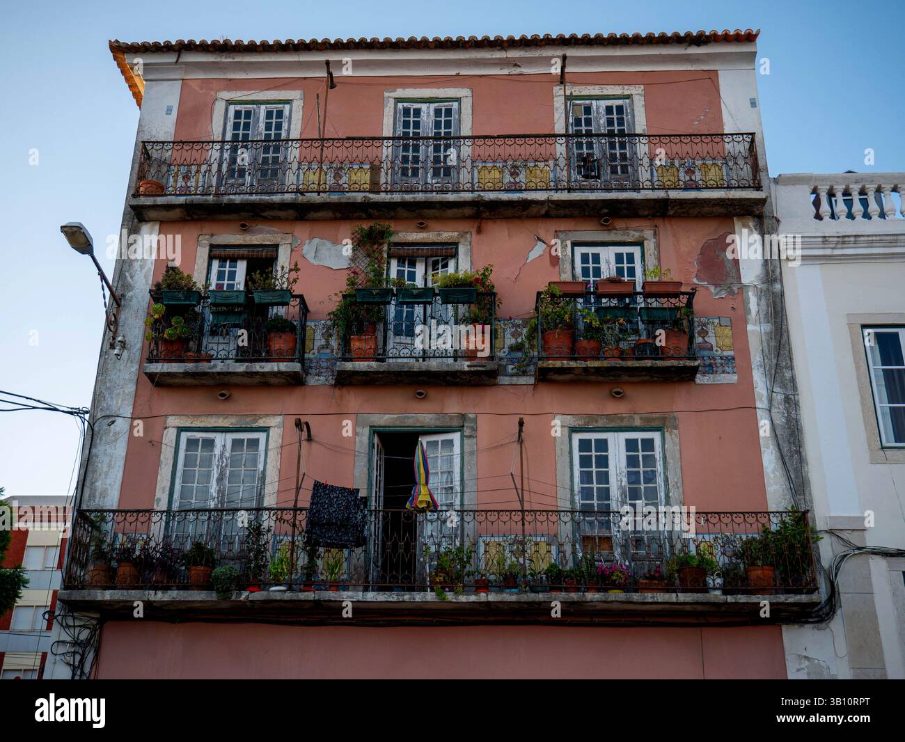 Un charmant bâtiment européen avec une façade rose et trois étages de caractère, chacun avec des balcons confortables débordant de plantes verdoyantes Banque D'Images